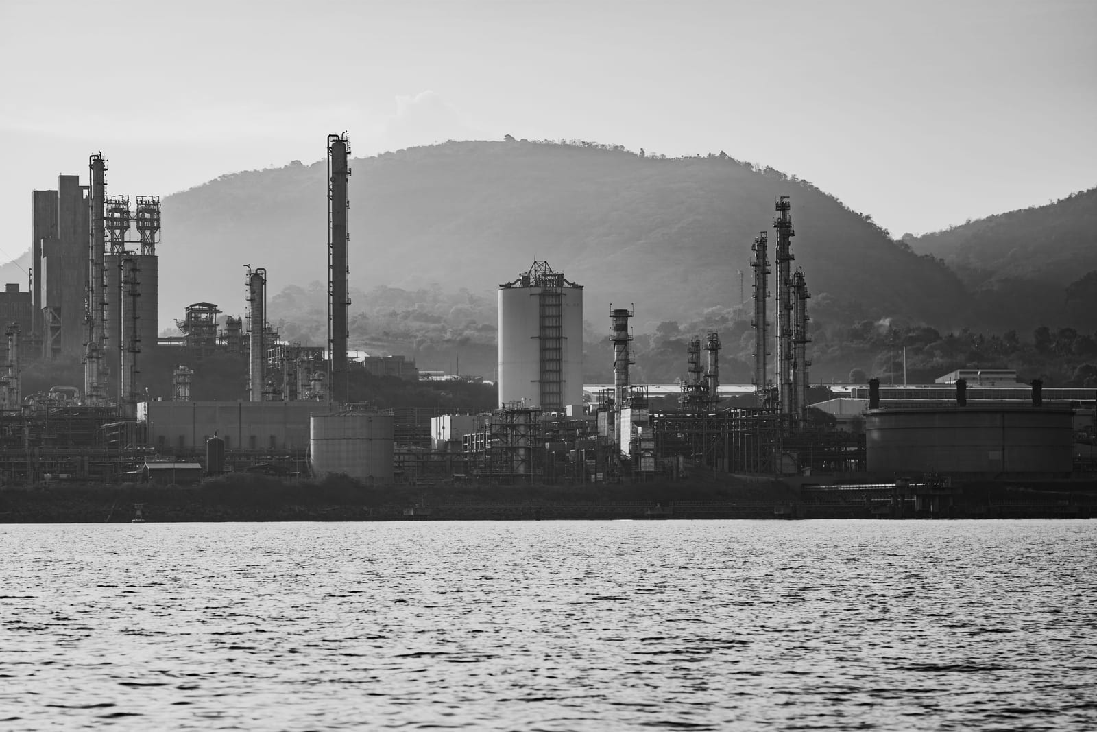 Industrial refinery on a waterfront, seen from across the water with hills behind it